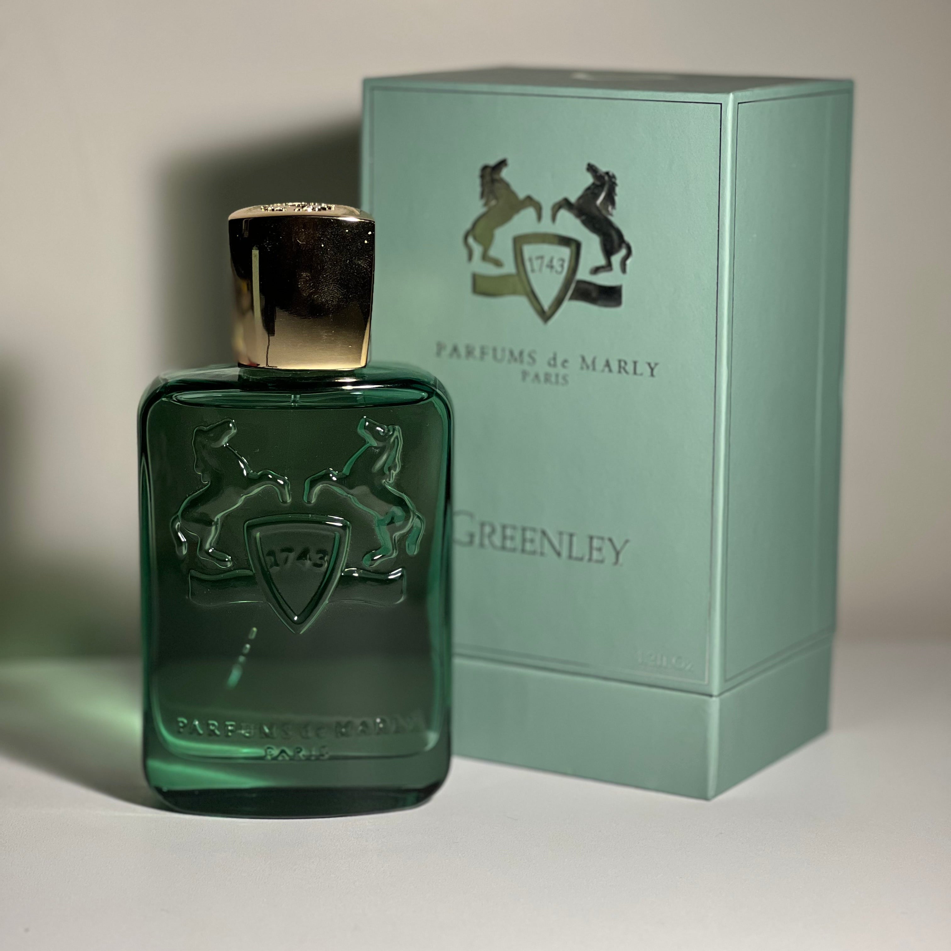 Green perfume bottle with gold cap and matching box from Parfums de Marly on a neutral background